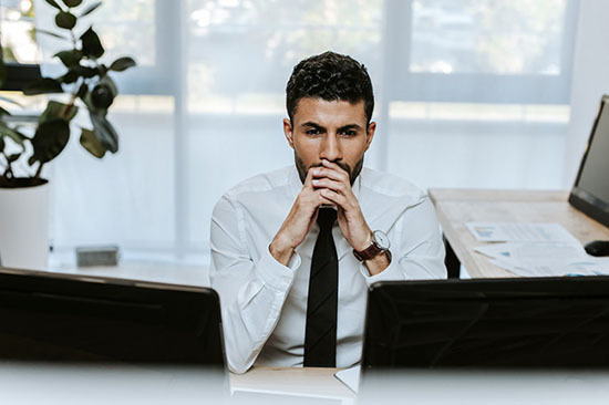 Business man in front of two computers, worried about cybersecurity.